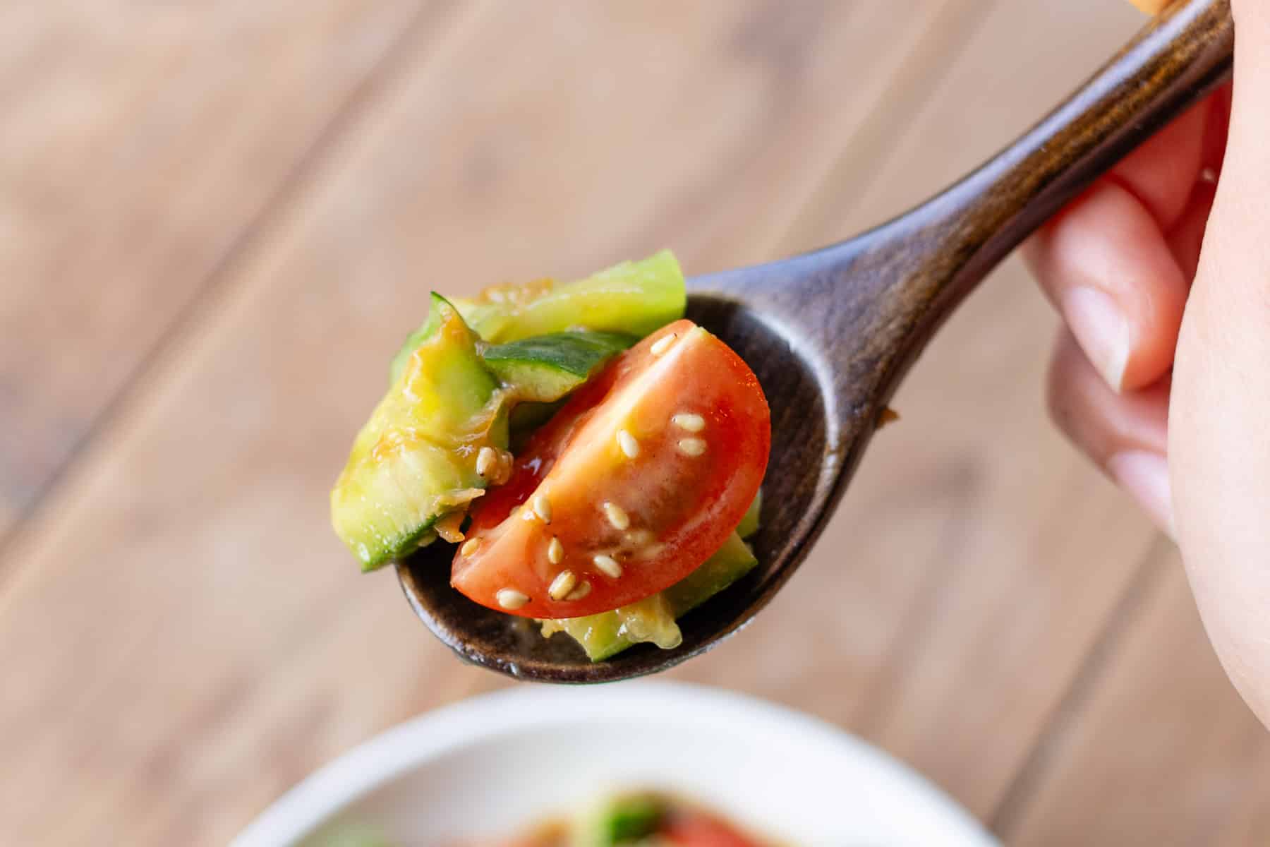 A spoonful of smashed sesame cucumber salad with a tomato garnished with sesame seeds.