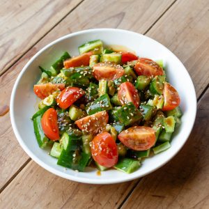 a plate of smashed sesame cucumber salad with tomatoes and garnished with sesame seeds.