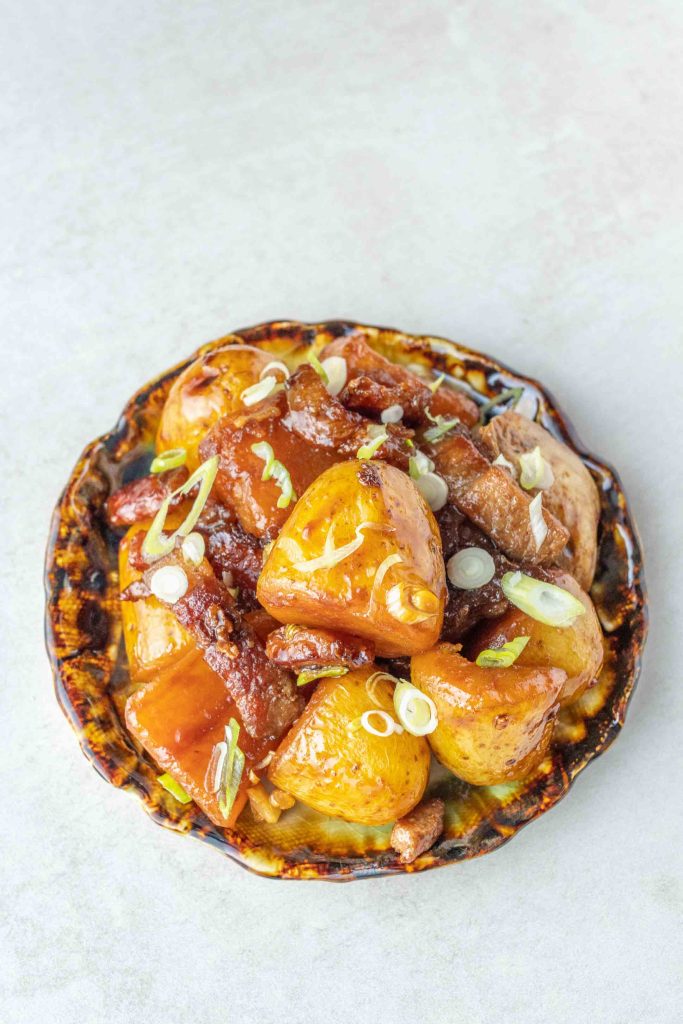 Japanese Pork and Potato (Nikkujaga) on a small side dish plate, garnished with spring onions.