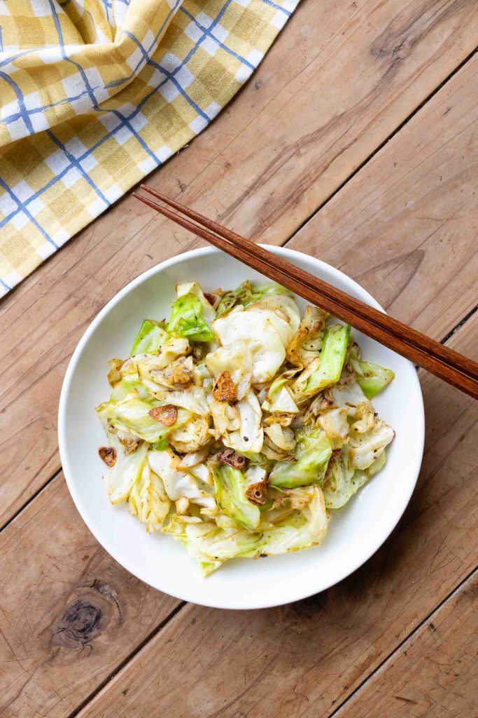 A plate of stir fried cabbage with pieces of garlic. 