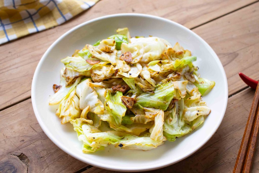 A plate of stir fried cabbage with pieces of garlic.