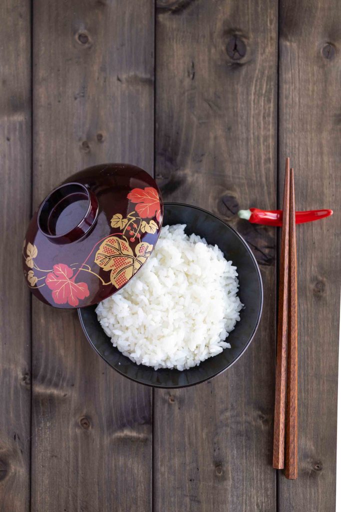 A bowl of white rice with some chopsticks on the side.