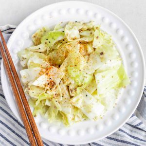 A plate of Yamitsuki Cabbage on top of a striped dishcloth with some chopsticks laying on the side.