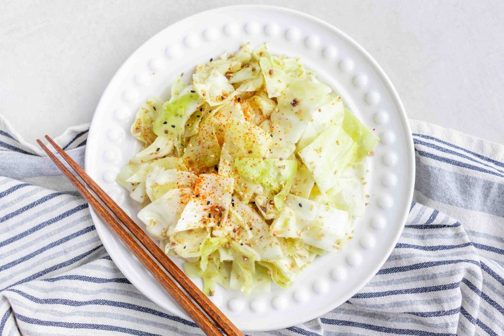 A plate of Yamitsuki Cabbage on top of a striped dishcloth with some chopsticks laying on the side.