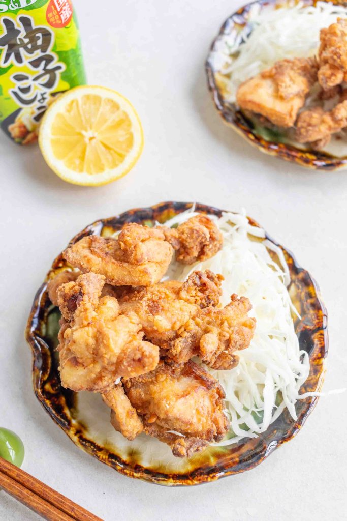 A plate of Yuzu Kosho Fried Chicken on a small plate. In the background there is half a lemon and a bottle of Yuzu Kosho.