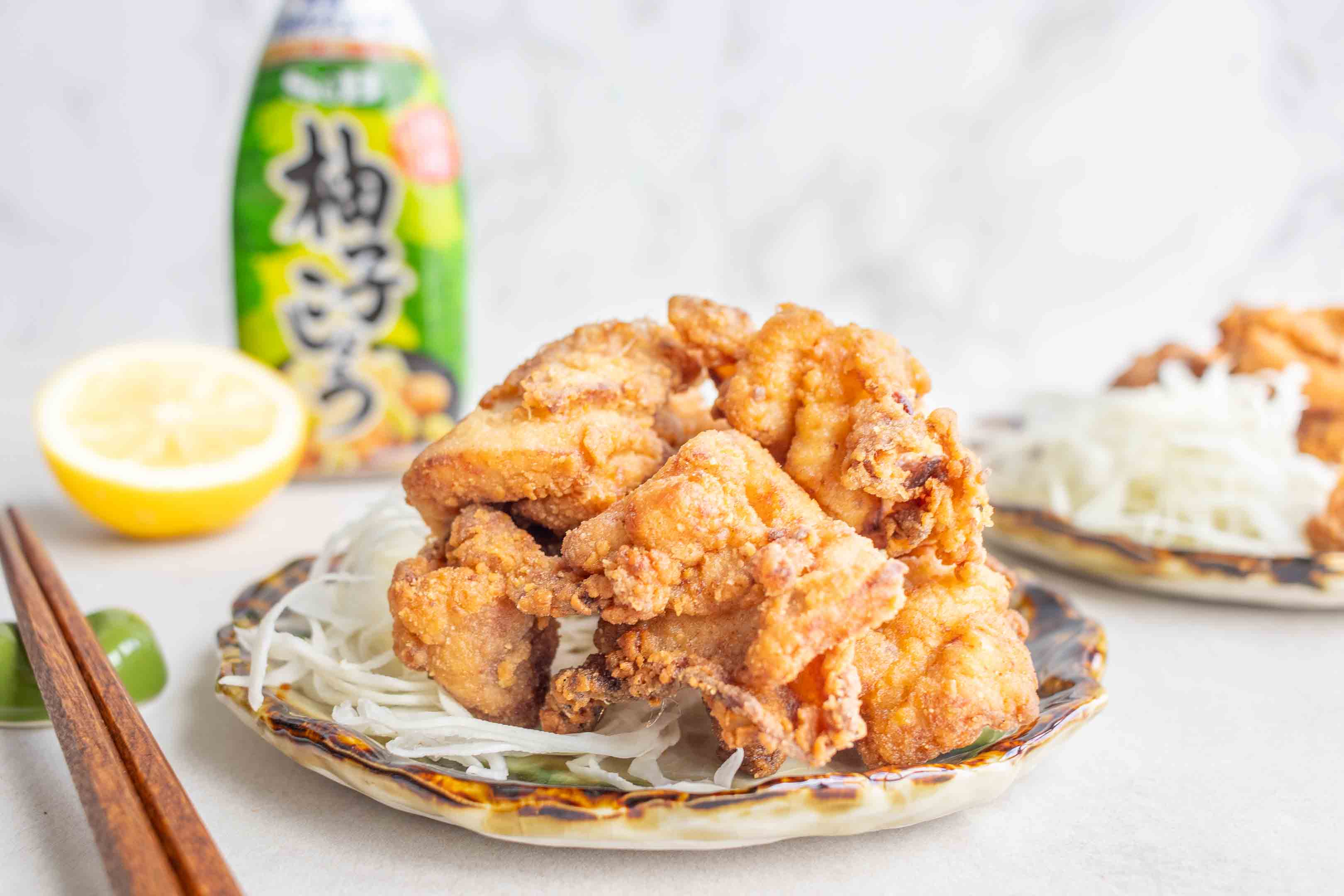 A plate of Yuzu Kosho Fried Chicken on a small plate. In the background there is half a lemon and a bottle of Yuzu Kosho.