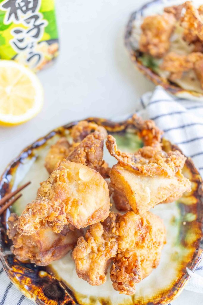 A plate of Yuzu Kosho Fried Chicken on a small plate. In the background there is half a lemon and a bottle of Yuzu Kosho.