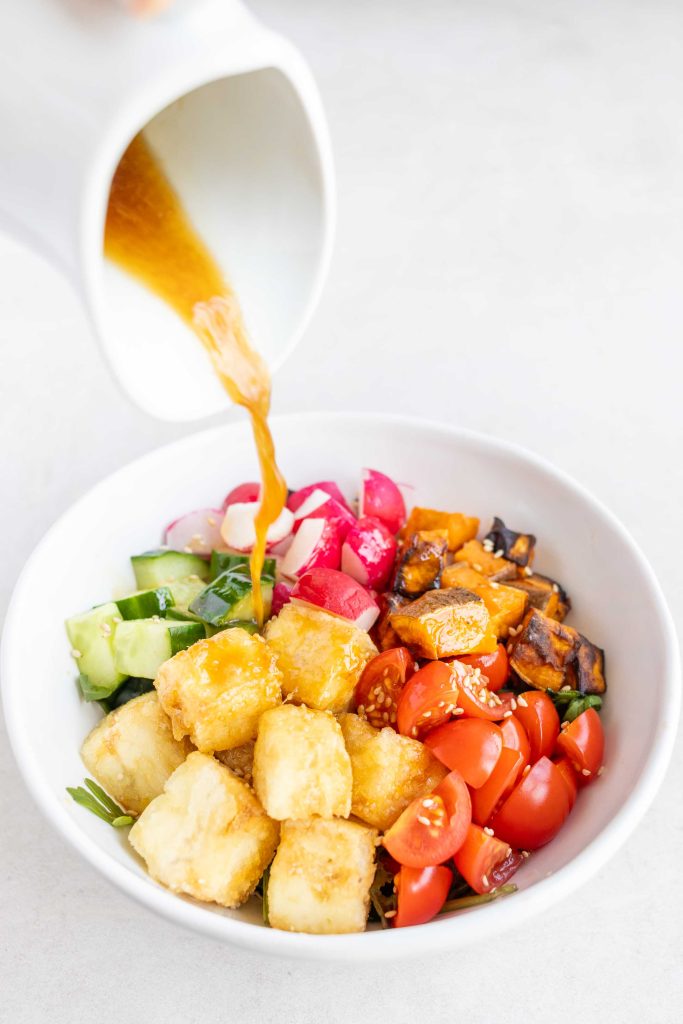 Salad dressing being poured onto a bowl of Japanese Tofu Salad.
