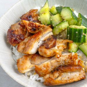 A close up of a bowl of miso chicken thighs chopped up with some smashed cucumbers, all on top of some white rice.