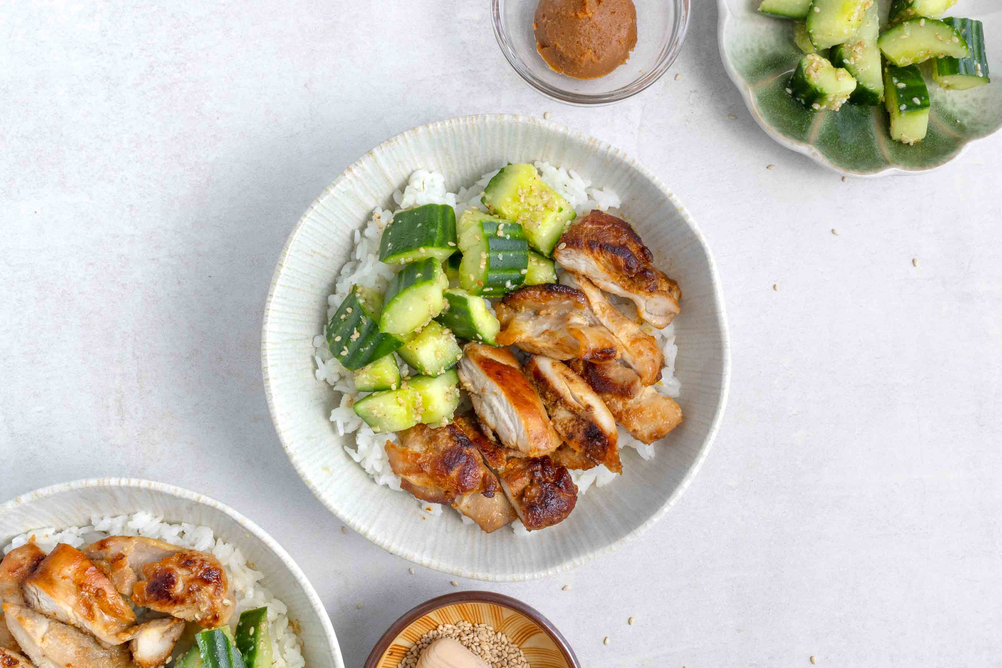 A bowl of miso chicken thighs chopped up with some smashed cucumbers, all on top of some white rice.