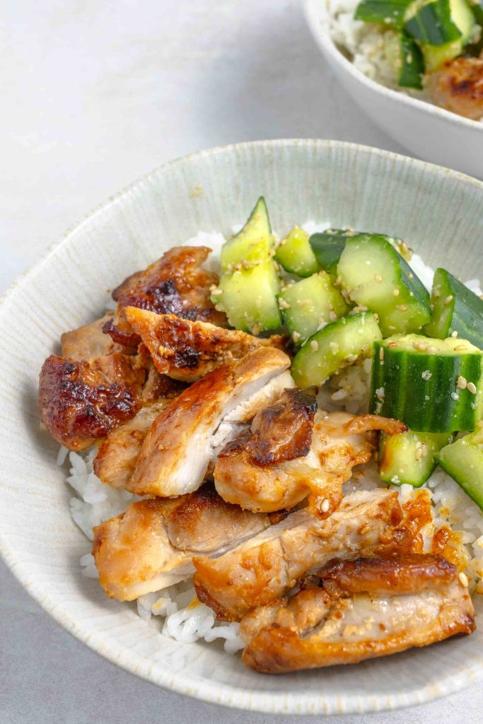 A close up of a bowl of miso chicken thighs chopped up with some smashed cucumbers, all on top of some white rice.