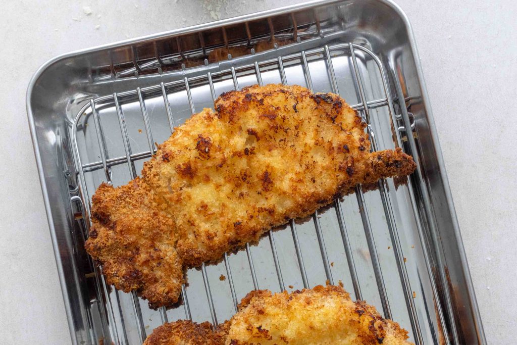A piece of air fryer pork katsu on a silver cooling rack.