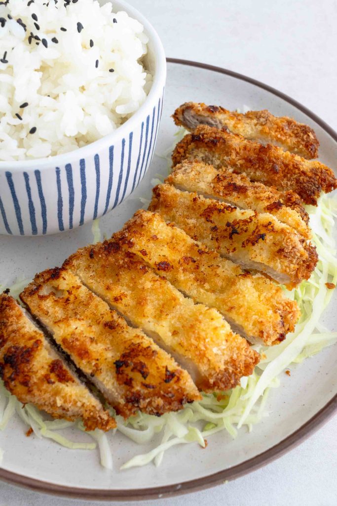 A piece of air fryer pork katsu sliced and placed on top of a bed of cabbage.