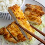 A piece of air fryer pork katsu being held up by wooden chopsticks.