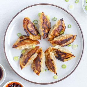 A plate of Gyoza with a side of dipping sauce and chilli oil. Sprinkled with some spring onion.