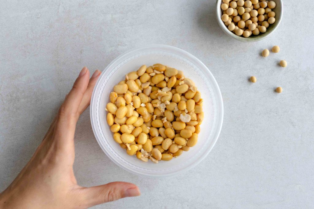 A pot of homemade natto with a hand reaching to grab it.