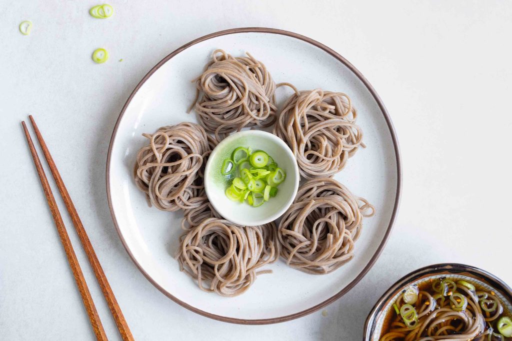 A plate of Zaru Soba with spring onion for garnish and some chopsticks to the right.