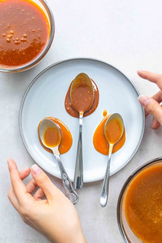 A pair of hands placing down a plate with three spoons covered with miso caramel.