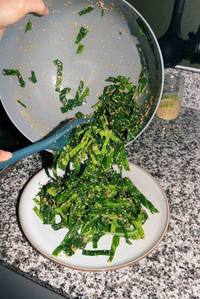 A bowl of Goma-ae Spring Greens being transferred to a plate.