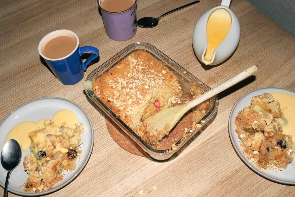 A dish of Kinako Mochi Apple Crumble surrounded by plates of crumble and custard.