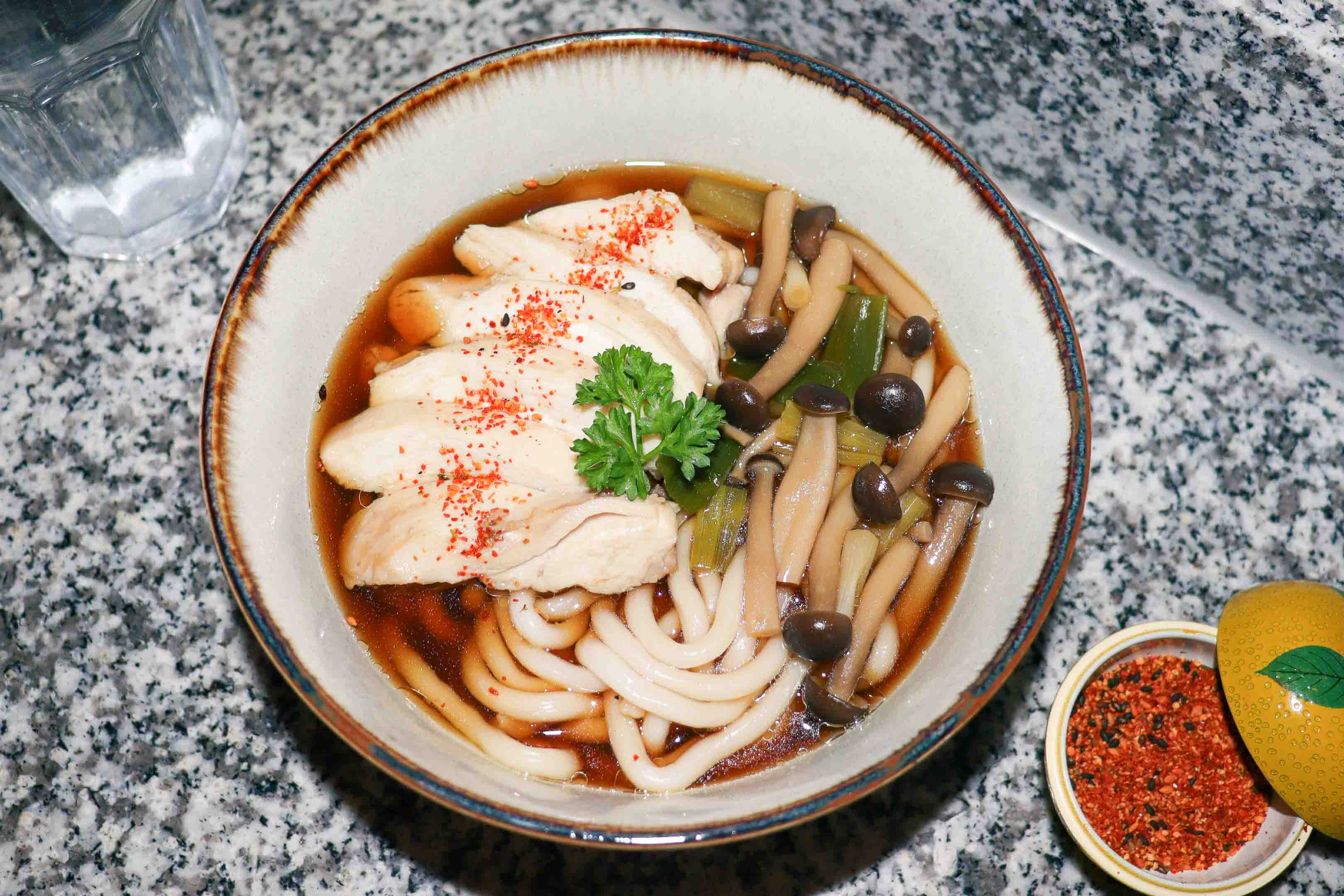 A bowl of Chicken Udon Noodle Soup with mushrooms and a sprinkle of shichimi.